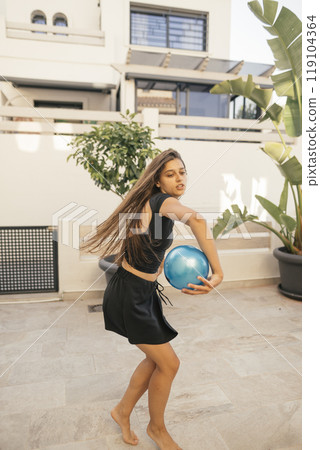 A young girl is joyfully playing with a colorful bowling ball in a sunny outdoor setting A young girl is joyfully playing with a colorful bowling ball in a sunny outdoor setting 119104364