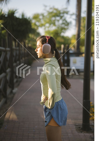 A young woman is enjoying her leisure time outdoors while wearing headphones and relaxing A young woman is enjoying her leisure time outdoors while wearing headphones and relaxing 119104391