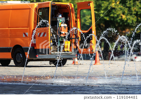 Orange utility service van doors open parked near working fountain in city street center. Fountain system maintenance, inspection winterization work. Equipment tools water accident emergency  vehicle 119104481