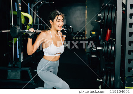 Asian woman muscular guy squat exercise with a lifting barbell in gym, female exercising squatting performing shoulder press lift weight for legs at fitness gym, workout healthy lifestyle concept Asian woman muscular guy squat exercise with a lifting barbell in gym, female exercising squatting performing shoulder press lift weight for legs at fitness gym, workout healthy lifestyle concept 119104601