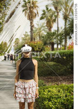 A young woman in VR gear explores a beautiful tropical landscape, enjoying her adventure A young woman in VR gear explores a beautiful tropical landscape, enjoying her adventure 119104736