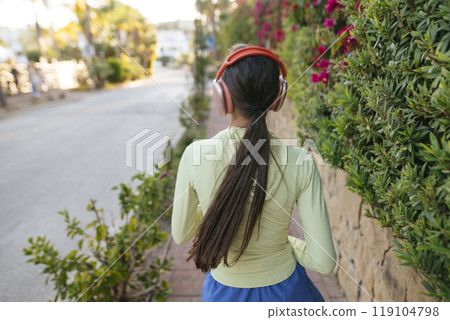 A girl is walking outdoors with her headphones on in a vibrant and colorful environment A girl is walking outdoors with her headphones on in a vibrant and colorful environment 119104798