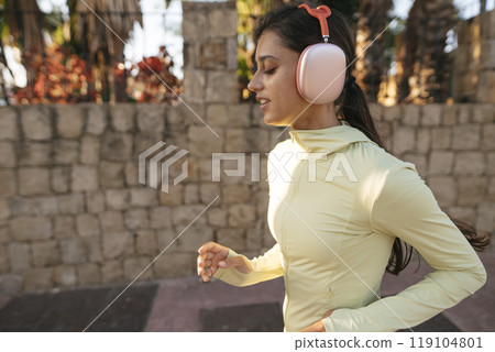 A young woman is jogging outdoors while wearing stylish ear muffs for added warmth and comfort 119104801