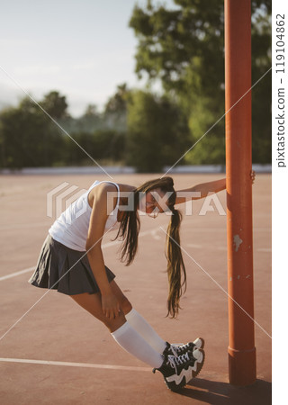 A Sporty and Energetic Young Woman Confidently Posing on a Tennis Court Under the Sunlight 119104862
