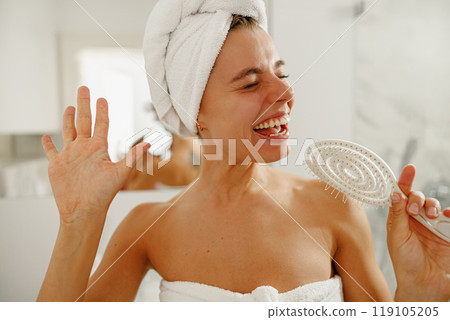 A Joyful Woman Happily Singing in Her Bathroom While Wearing a Hair Towel on Her Head A Joyful Woman Happily Singing in Her Bathroom While Wearing a Hair Towel on Her Head 119105205