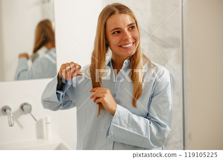 A cheerful woman is smiling while she brushes her hair in a cozy, welllit bathroom setting 119105225