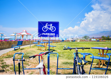 Bicycles are parked on a land lot next to a sign that says parking, as the blue sky and white clouds make a beautiful natural landscape 119106026