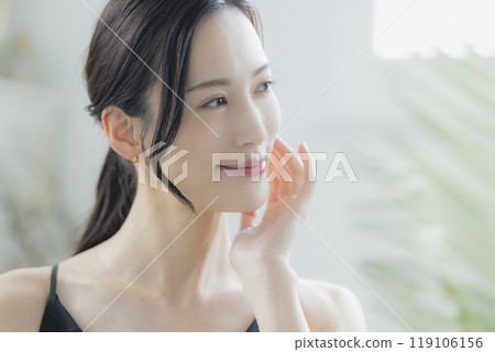 A woman in a black camisole dress standing by the window 119106156