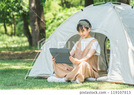 一個女孩在露營地/休閒設施的帳篷裡使用平板電腦 一個女孩在露營地/休閒設施的帳篷裡使用平板電腦 119107813