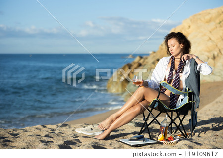 Businesswoman with glass of whiskey on seashore Businesswoman with glass of whiskey on seashore 119109617