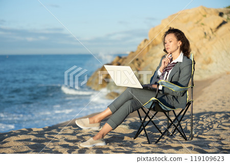 Businesswoman in office clothes working on laptop on seashore 119109623