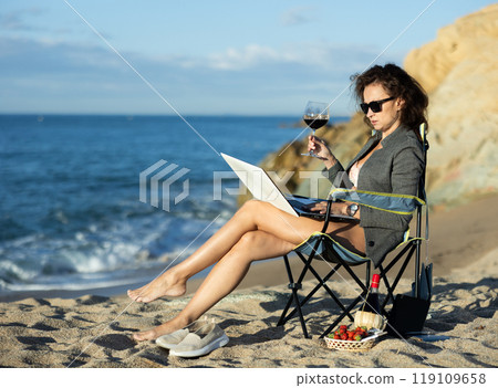 Sexy businesswoman drinking wine while working on beach 119109658
