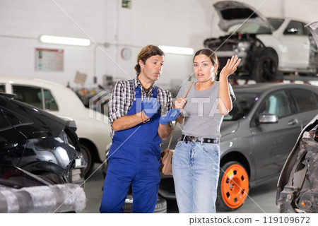 Experienced mechanic discussing car repair with worried female customer 119109672