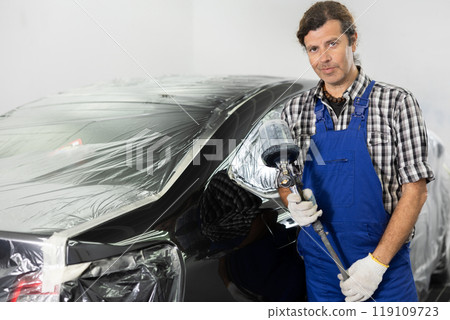 Adult male mechanic paints car with machine Adult male mechanic paints car with machine 119109723
