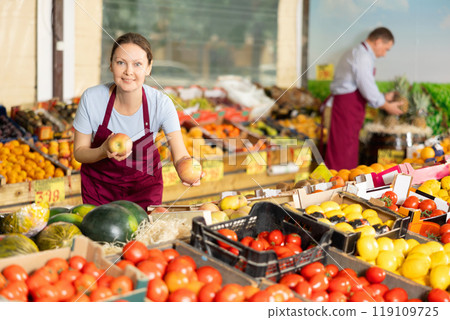 Friendly saleswoman offering fresh apples in greengrocery store Friendly saleswoman offering fresh apples in greengrocery store 119109725
