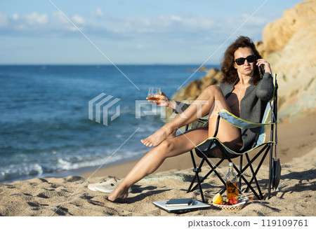Tempting businesswoman drinking whiskey and talking on phone on beach Tempting businesswoman drinking whiskey and talking on phone on beach 119109761