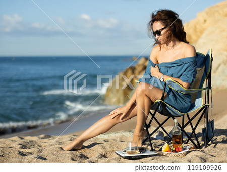 Relaxed naked woman in blue robe enjoying privacy on ocean beach 119109926