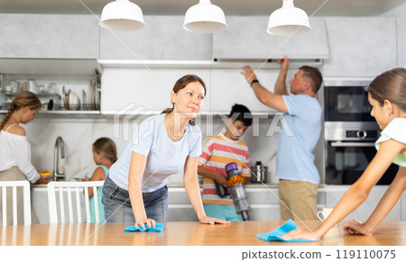 Daughters with mom wipe table, dad and brother do kitchen household chores in background Daughters with mom wipe table, dad and brother do kitchen household chores in background 119110075