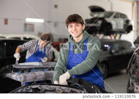 Positive young auto mechanic working in car repair workshop 119110076