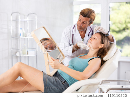Adult male doctor examining face of female patient 119110220