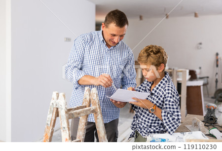 Little son with father together checking blueprints before renovating room Little son with father together checking blueprints before renovating room 119110230