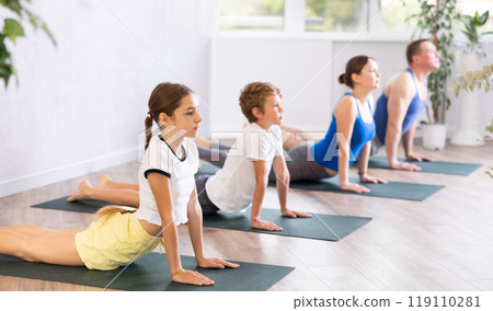 Pleasant preteen girl practicing cobra pose of yoga with her family Pleasant preteen girl practicing cobra pose of yoga with her family 119110281