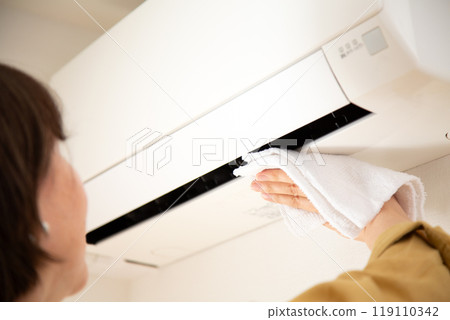 A middle-aged woman wiping and cleaning an air conditioner A middle-aged woman wiping and cleaning an air conditioner 119110342