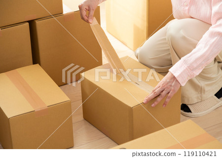 A middle-aged woman opening a cardboard box containing moving luggage A middle-aged woman opening a cardboard box containing moving luggage 119110421