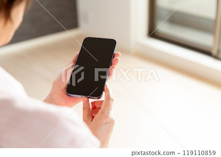 A middle-aged woman looking at her smartphone during an apartment viewing 119110859