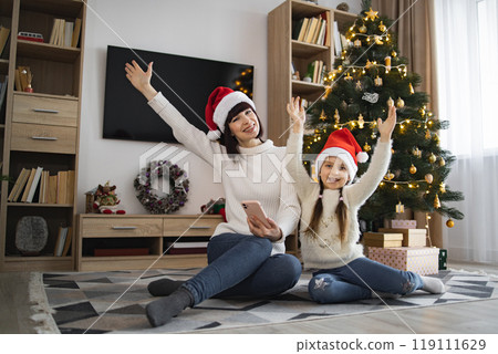 Mother and daughter enjoying Christmas together with phone near tree 119111629