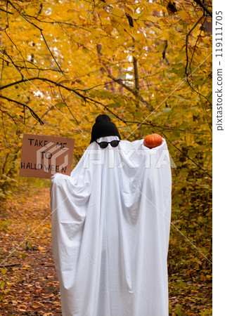 Trendy halloween celebration outdoors in autumn time. Handmade ghost costume from sheets, cap and glasses. Fall forest Trendy halloween celebration outdoors in autumn time. Handmade ghost costume from sheets, cap and glasses. Fall forest 119111705