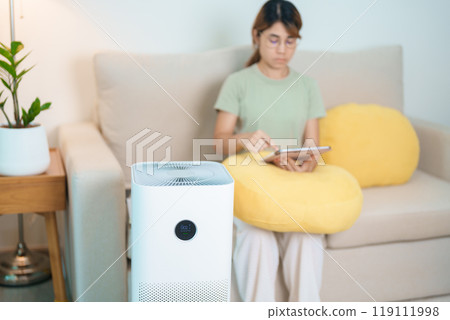 Air Purifier with woman relax and use tablet on sofa. Purification system for filter and cleaning dust PM2.5 HEPA and virus in home. Allergy, Pure air, health, Wellness lifestyle and Air Pollution 119111998