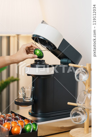 hand making Espresso Coffee by Coffee Maker Machine with Capsule of roasted coffee bean on wood table bar. Daily beverage drink at Home, Apartment and Office concept hand making Espresso Coffee by Coffee Maker Machine with Capsule of roasted coffee bean on wood table bar. Daily beverage drink at Home, Apartment and Office concept 119112034