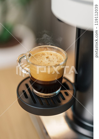 Espresso cup with steam and froth during Coffee making Coffee by Coffee Maker Machine on wood table bar. Cafe shop, Daily beverage drink at Home, Apartment and Office concept Espresso cup with steam and froth during Coffee making Coffee by Coffee Maker Machine on wood table bar. Cafe shop, Daily beverage drink at Home, Apartment and Office concept 119112039