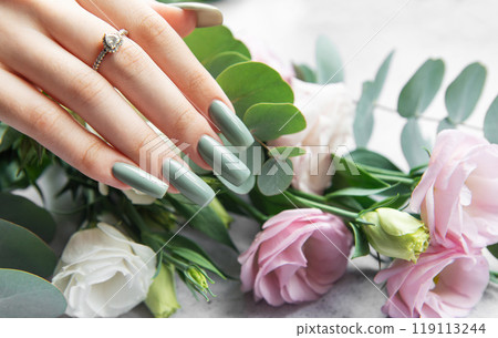 Elegant hand adorned with a ring showcasing stylish green nails beside a bouquet Elegant hand adorned with a ring showcasing stylish green nails beside a bouquet 119113244