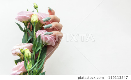A hand holding soft pink flowers with green accents against a white background A hand holding soft pink flowers with green accents against a white background 119113247