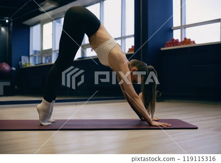 Yoga practitioner performing downward dog pose in a modern fitness studio 119115316