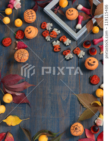 Frame of fall leaves, candy for Halloween. Holidays and food. Dessert in the shape of a pumpkin, skull, witch. Background for design.  119115486
