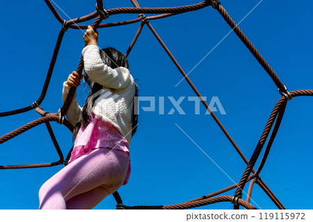 A toddler playing on a rope jungle gym, face not visible, against a clear, cloudless blue sky A toddler playing on a rope jungle gym, face not visible, against a clear, cloudless blue sky 119115972