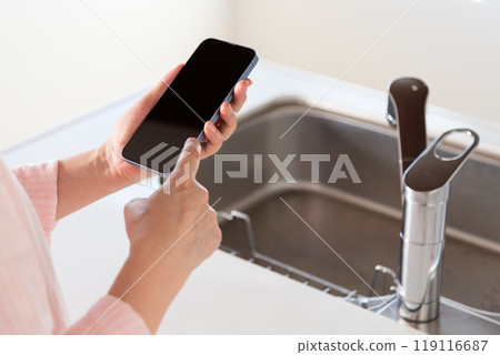 有檯面廚房水槽和智慧型手機的中年婦女 119116687