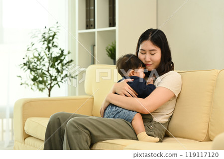 Loving young mother cuddling her baby boy sitting on sofa. Parenting, childcare and family concept Loving young mother cuddling her baby boy sitting on sofa. Parenting, childcare and family concept 119117120