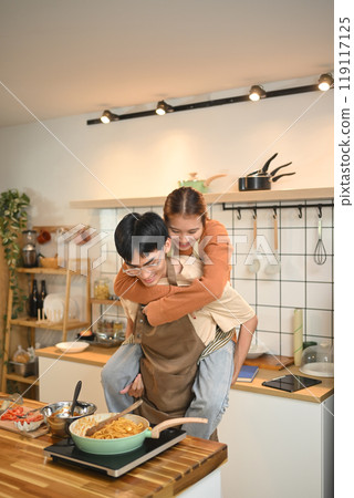 Playful young couple preparing meal and sharing a romantic moment in kitchen Playful young couple preparing meal and sharing a romantic moment in kitchen 119117125