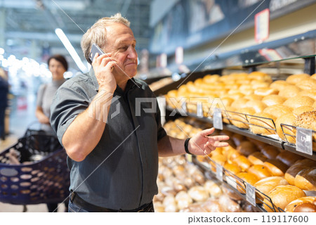 Man takes muffins on shelf of bakery section 119117600
