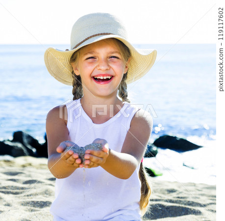 Baby girl in hat playing with sand on sea coast in summer Baby girl in hat playing with sand on sea coast in summer 119117602