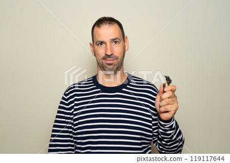 Bearded hispanic man in his 40s wearing a striped sweater with an electric razor preparing to shave, isolated over beige background. 119117644