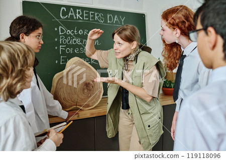Joyful female forester standing in classroom telling about dendrochronology during career guidance class at school 119118096