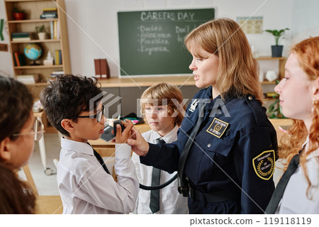 Female police officer teaching kids how to use walkie-talkie while speaking about her occupation on career day at school Female police officer teaching kids how to use walkie-talkie while speaking about her occupation on career day at school 119118119