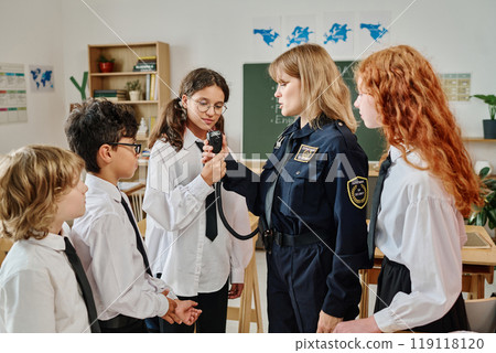 Female police office demonstrating portable radio transmitter to group of teenagers during vocational guidance class at school Female police office demonstrating portable radio transmitter to group of teenagers during vocational guidance class at school 119118120
