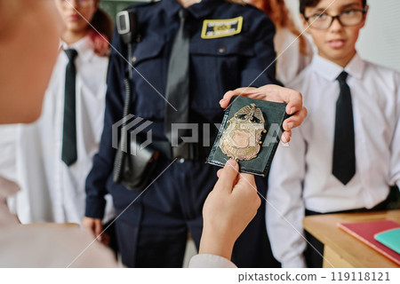 Unrecognizable female office showing her police badge to kids during career guidance class at school Unrecognizable female office showing her police badge to kids during career guidance class at school 119118121