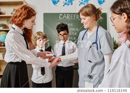 Red-haired teen girl learning how to use modern contactless electronic medical thermometer during career guidance class at school Red-haired teen girl learning how to use modern contactless electronic medical thermometer during career guidance class at school 119118149